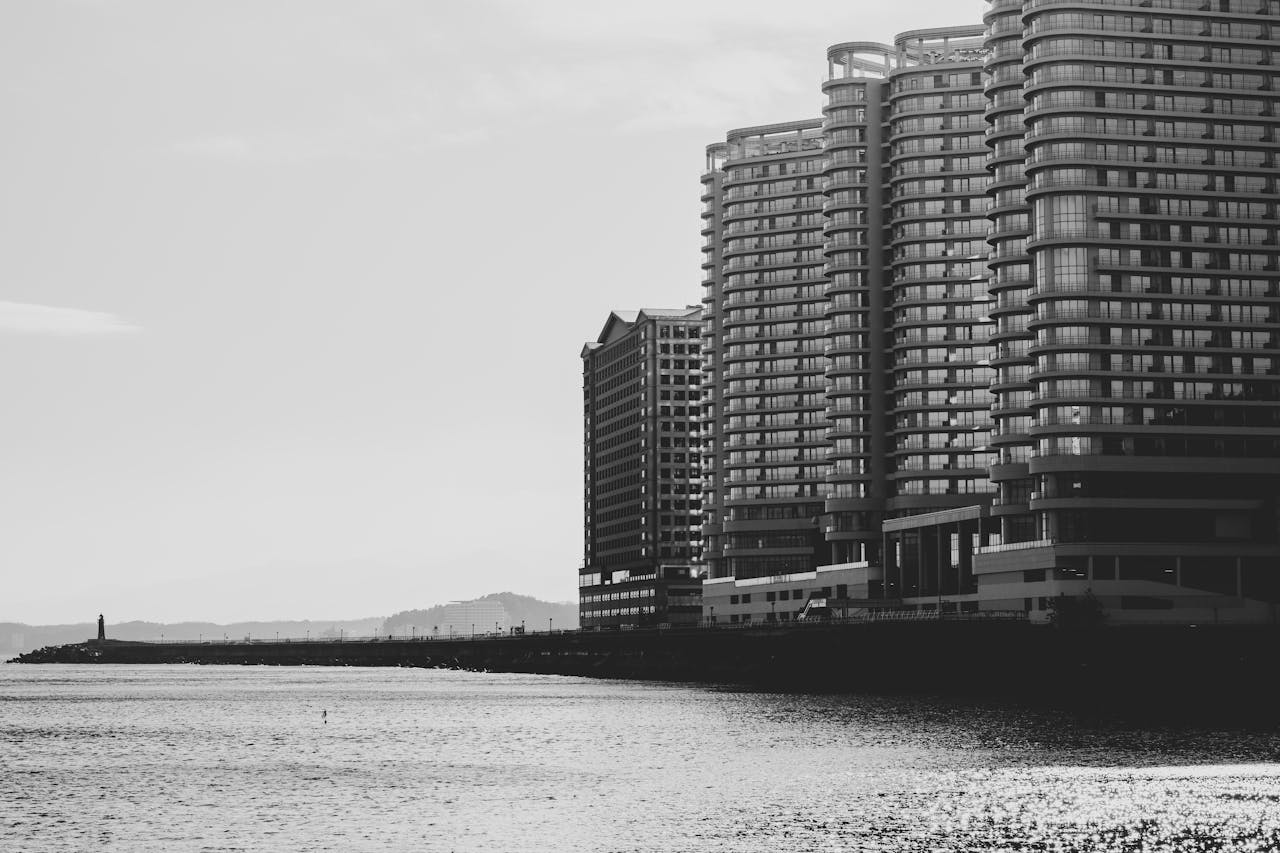 Monochrome image of modern high-rise buildings by a calm coastal waterfront.